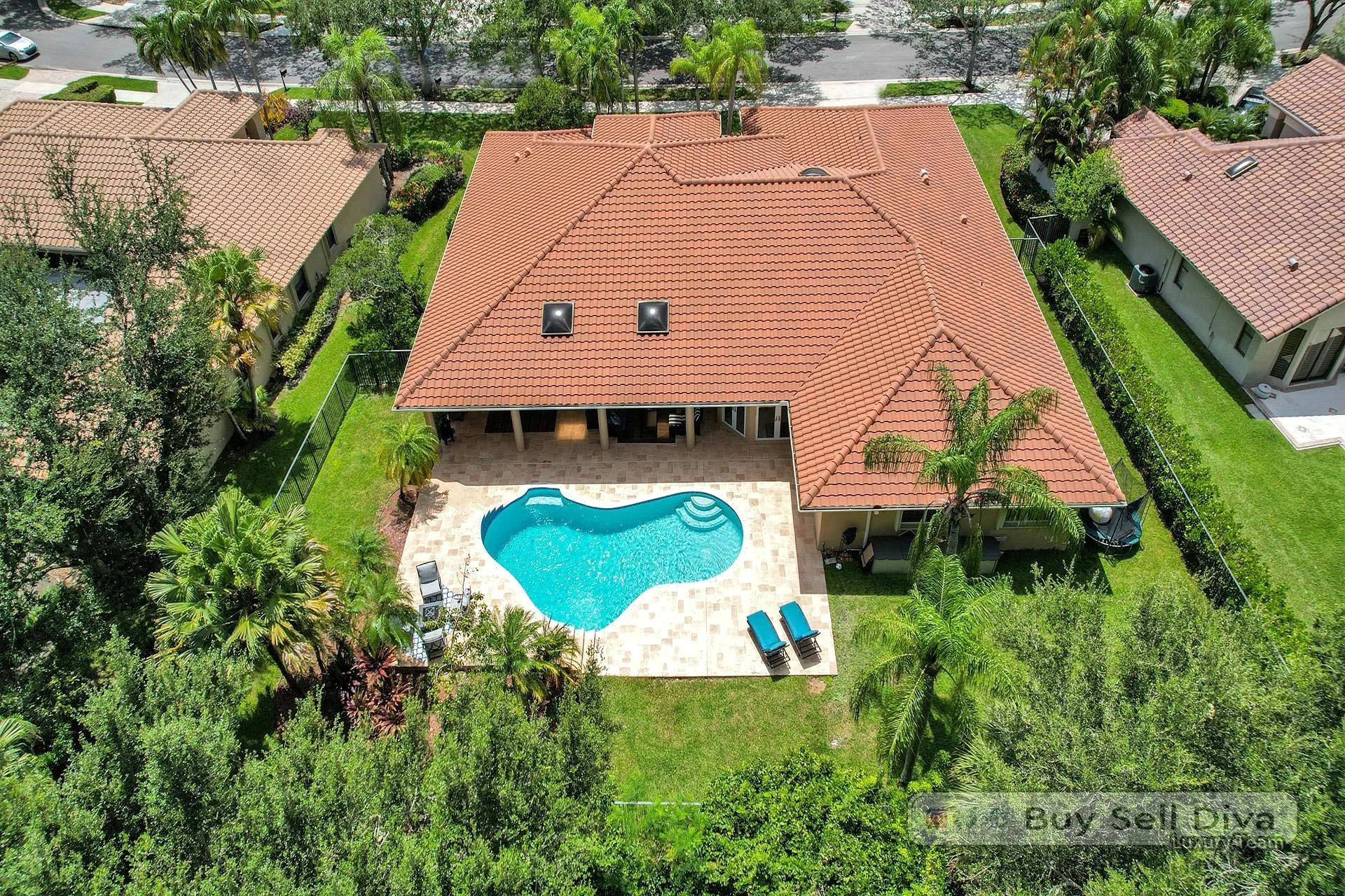 Aerial drone view of the oversized freeform pool and travertine deck behind the Weston Florida home