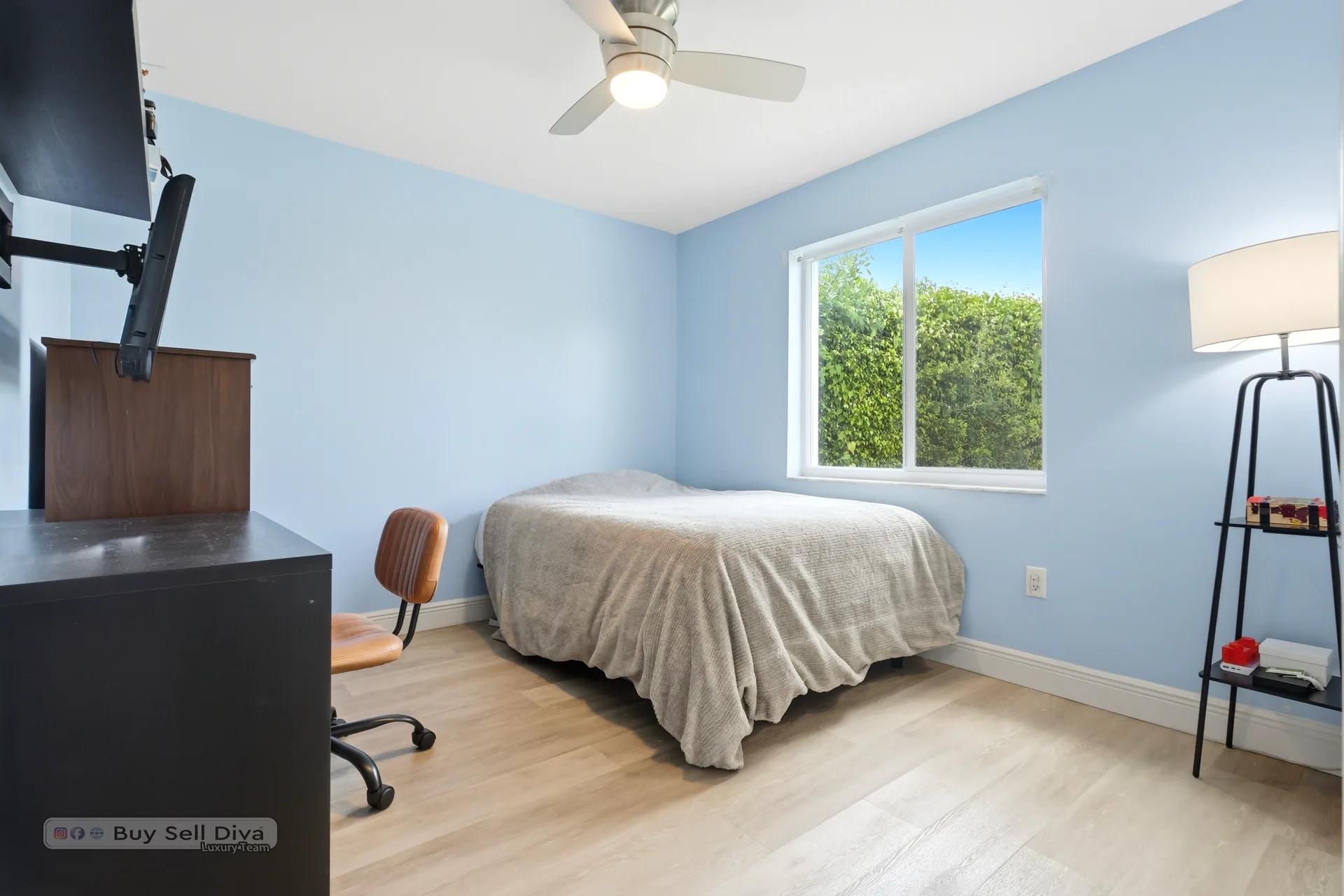 Secondary bedroom with ceiling fan and hedge-lined window view