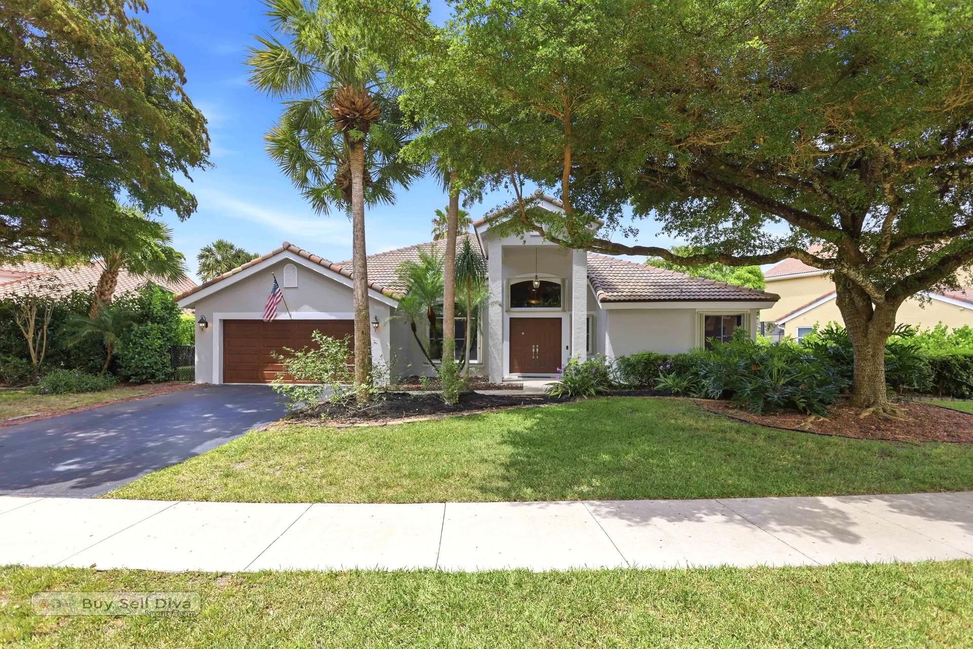 Front elevation with palms, mature shade tree, and two-car garage