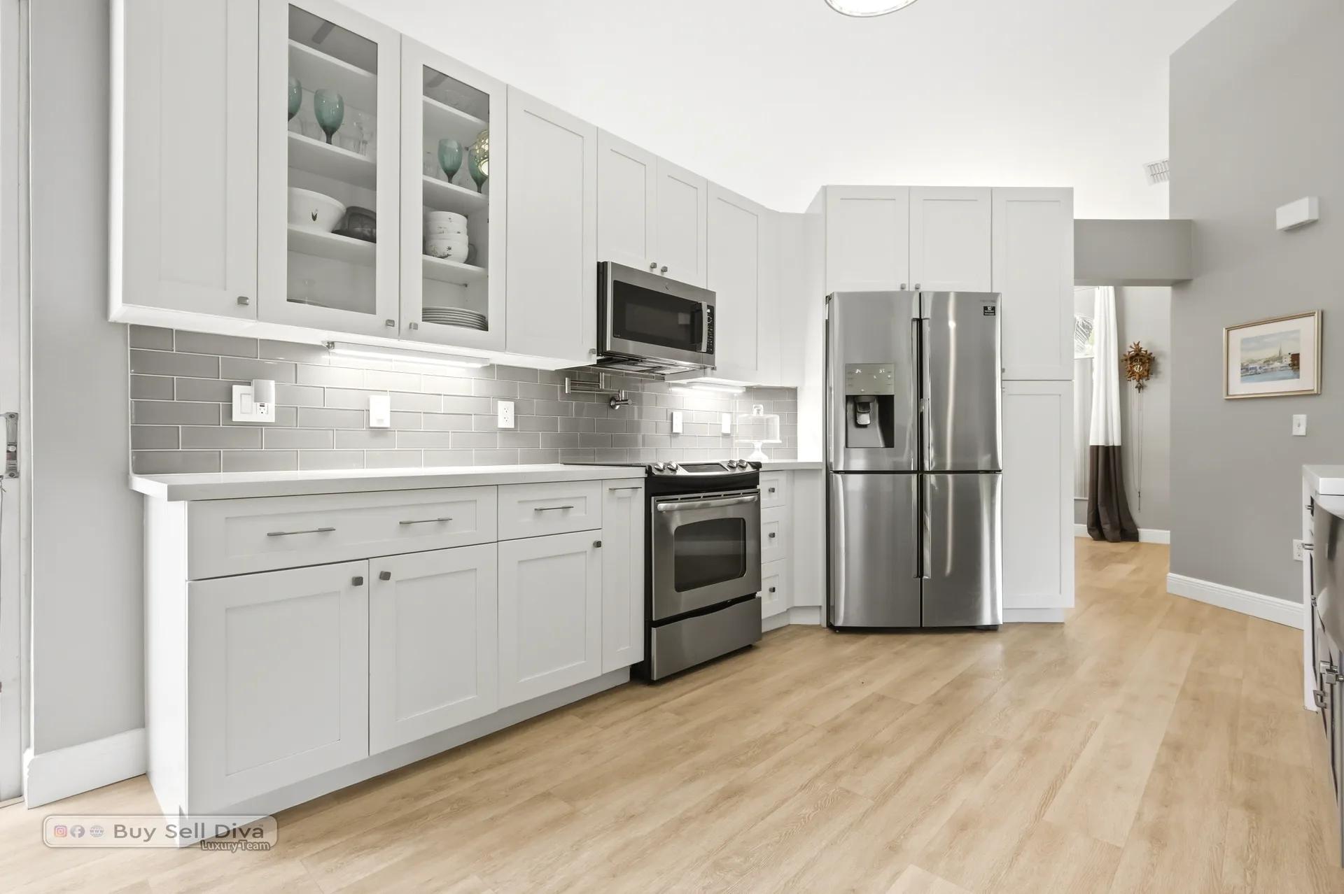 Remodeled white kitchen with stainless appliances and gray subway tile backsplash