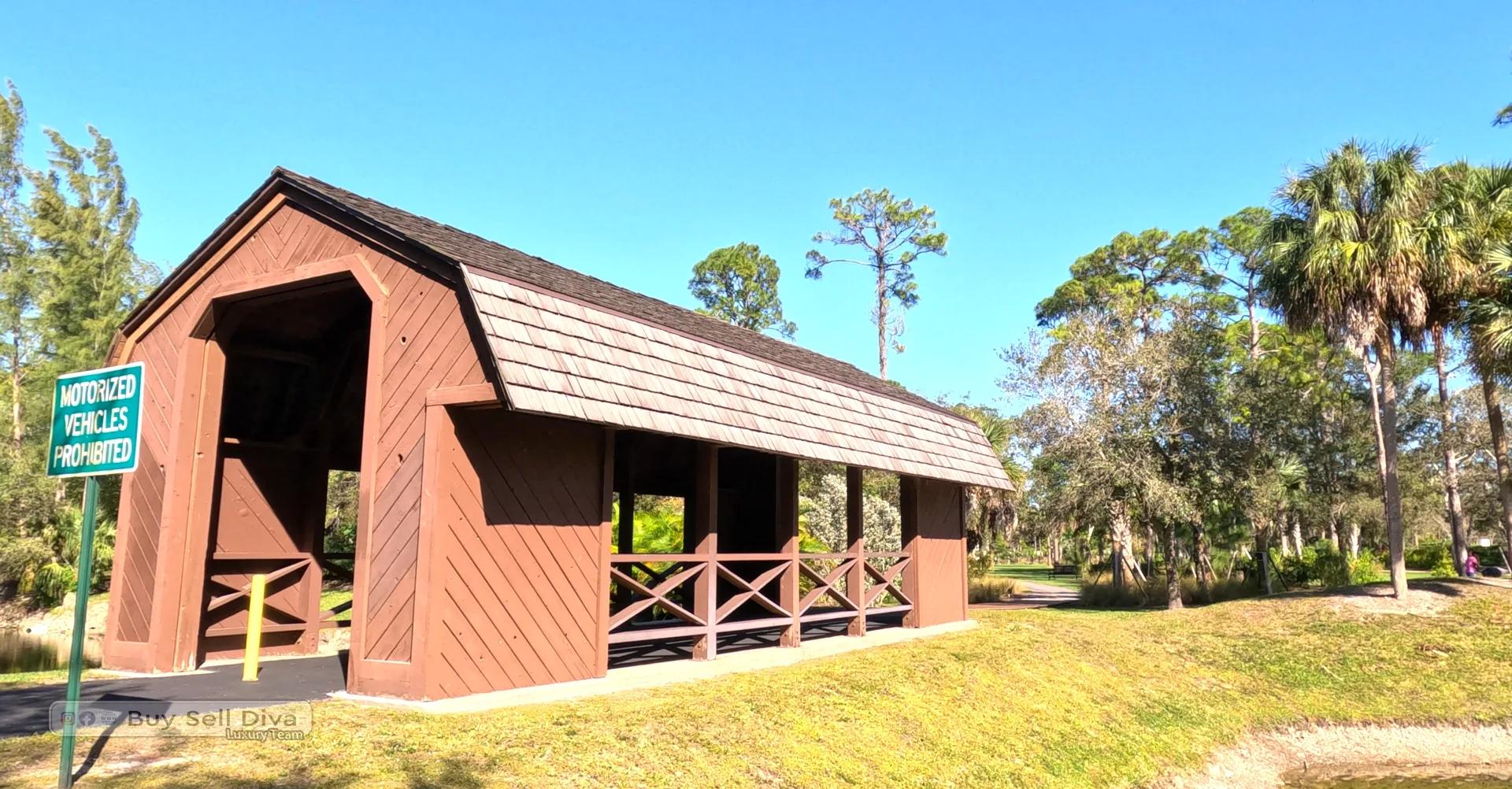 Covered wooden pedestrian bridge on a tree-lined nature trail framed by pines and palms in a Parkland, Florida park